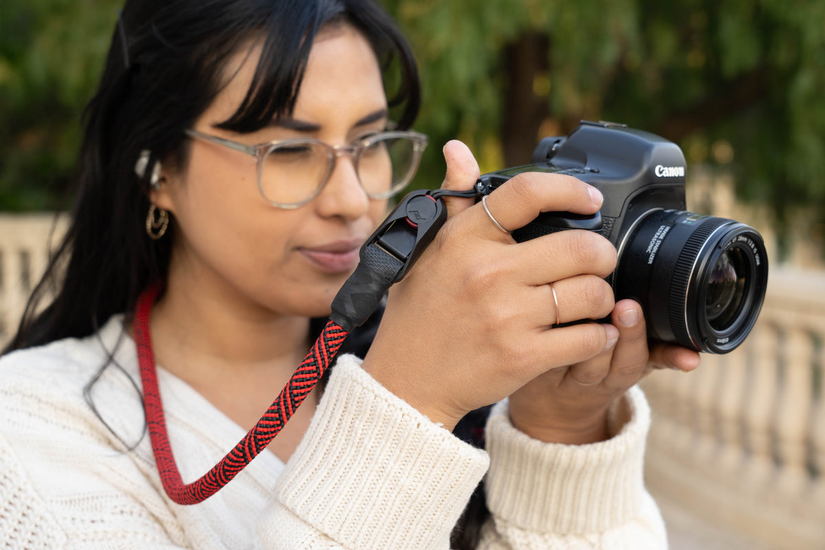Photographer holding a Canon camera with a red and black rope camera strap
